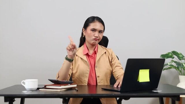 Adult business woman sitting at desk, working with laptop, serious expression with raised index finger gesture, sign of refusal or prohibition.