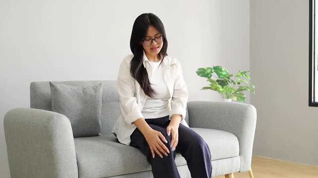 Young woman sitting on the sofa in the living room of the house, massaging her feet feeling sore, stiff and painful muscles or bones.