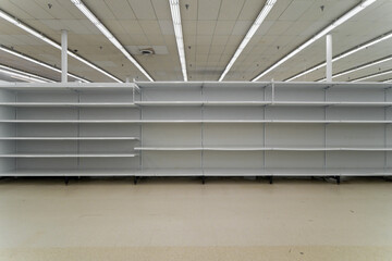 Wide frontal view of completely empty white metal supermarket gondola shelves stretching across a commercial retail store interior. © AncientAftertone