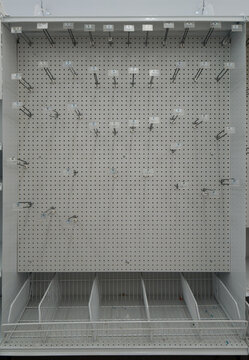 Completely empty retail pegboard stand rack with metal hooks and bottom wire baskets inside a commercial supermarket room.