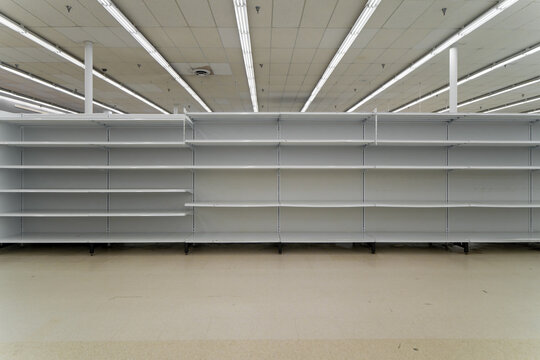 Wide frontal view of completely empty white metal supermarket gondola shelves stretching across a commercial retail store interior.