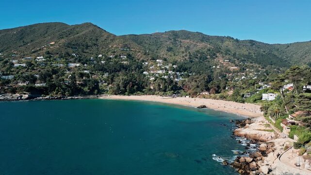 Sweeping panorama over deep blue bay revealing full crescent sandy beach and exclusive village with villas cascading down dense fore