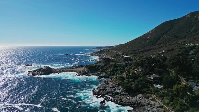Forward flight over dramatic rocky coastline with powerful waves crashing on reefs and exclusive villas tucked into steep native forested cliffs. Zapallar, Chile