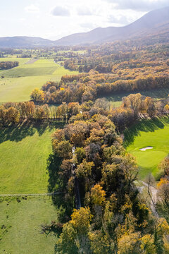 Aerial view of autumnal forests and green meadows with the Jura mountains in the background in La Rippe, Vaud, Switzerland.