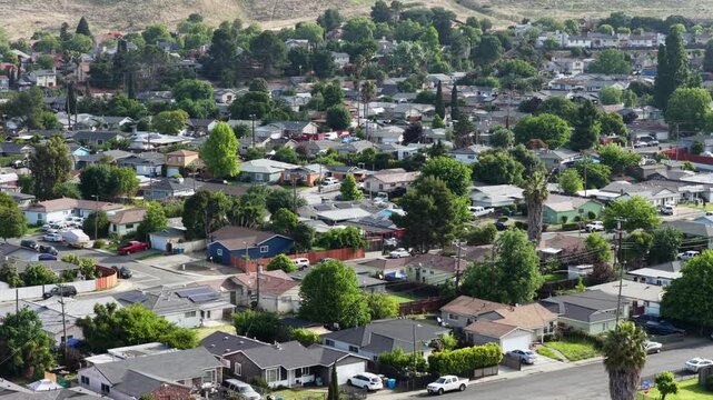 Vallejo residential neighborhood with single-family homes, solar panels and palm trees lining suburban streets, rolling hills and sprawl stretching to horizon. California, USA. Aerial wide shot.