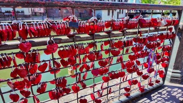 Red heart padlocks on railing of Pont du Faisan bridge with traditional houses in Strasbourg, France