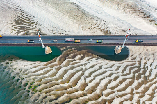Aerial view of Jamuna Bridge with vehicles crossing over the intricate sand patterns and turquoise water of the Jamuna River in Tangail District, Dhaka Division, Bangladesh.