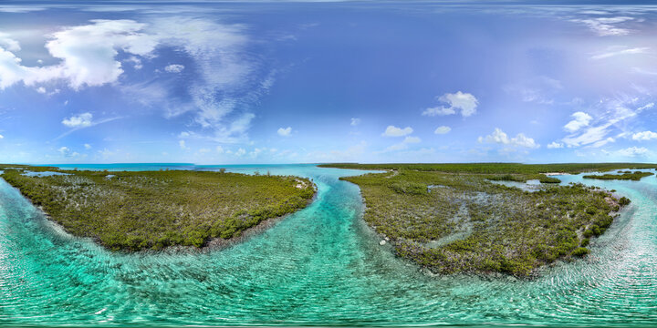 Aerial view of lush tropical islands and turquoise channels under a bright blue sky with scattered clouds William's Town, Exuma, The Bahamas.
