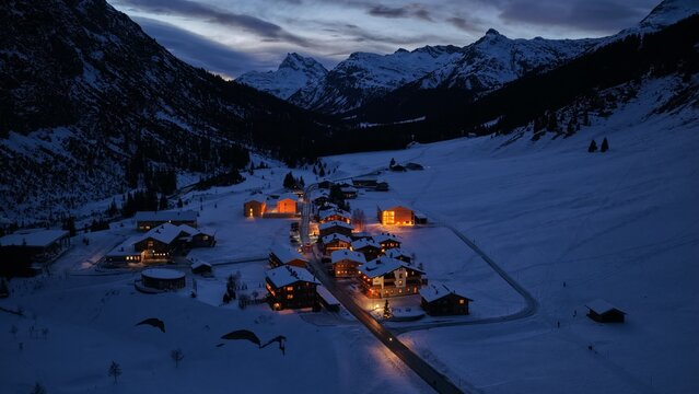 Aerial view of the snow-covered village of Lech am Arlberg with glowing lights from houses nestled among alpine peaks at twilight Lech am Arlberg, Vorarlberg, Austria.