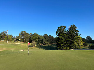 Obraz premium Scenic Golf Course Green with Red Checkered Flag Under Blue Sky