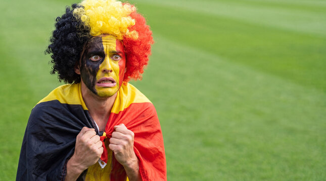 A distressed Belgian soccer fan with face paint and flag at stadium