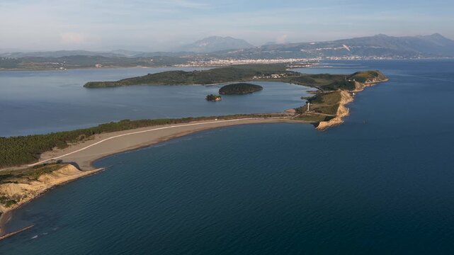 Aerial view of the long sandy beach and the calm waters of Narta Lagoon with Zvernec Island and distant mountains under a clear sky in Zvernec, Vlore County, Albania.