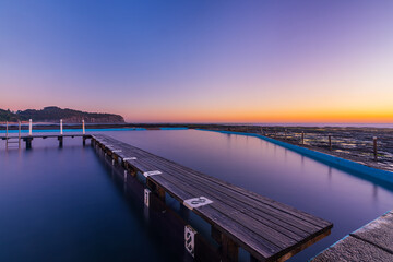 Fototapeta premium Calm sunrise over North Narrabeen Rockpool featuring smooth long exposure water, sandstone cliffs and pastel dawn colours on Sydney's Northern Beaches.