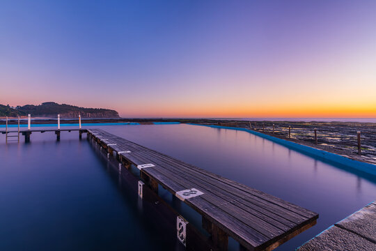 Calm sunrise over North Narrabeen Rockpool featuring smooth long exposure water, sandstone cliffs and pastel dawn colours on Sydney's Northern Beaches.