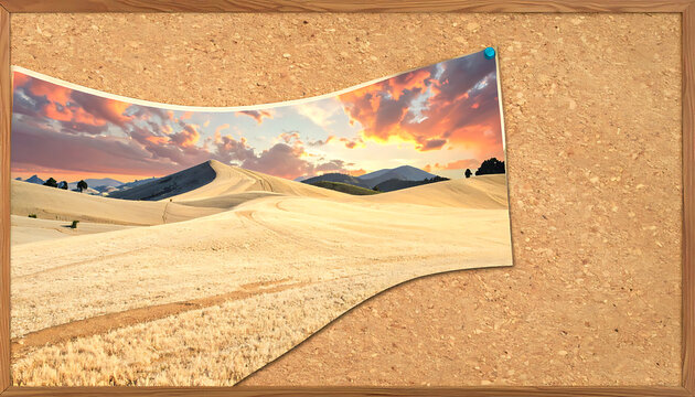 A picturesque landscape of rolling hills and fields under a dramatic sunset sky with colorful clouds, pinned to a corkboard