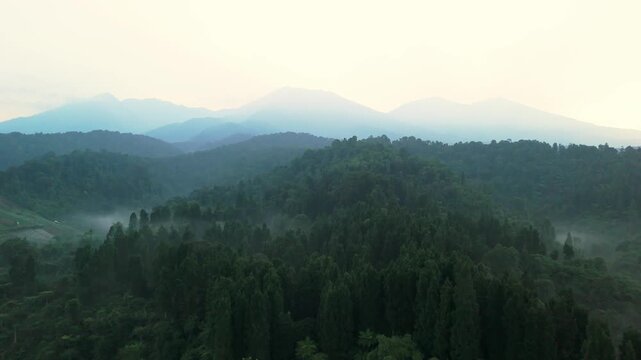 Aerial view of misty mountains and dense tropical forests during a hazy morning in Sukabumi, West Java, Indonesia.