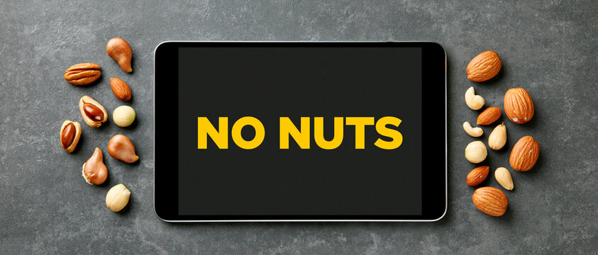 A smartphone displaying the text NO NUTS surrounded by various nuts on a dark, textured surface. The image emphasizes a prohibition or warning related to nuts.
