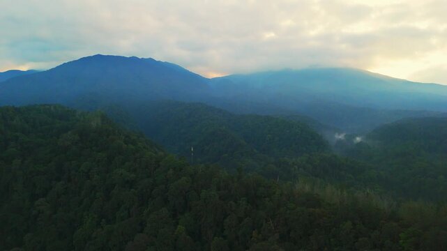 Aerial view of lush green mountains covered in dense tropical forest under a misty sky at dawn in Sukabumi, West Java, Indonesia.