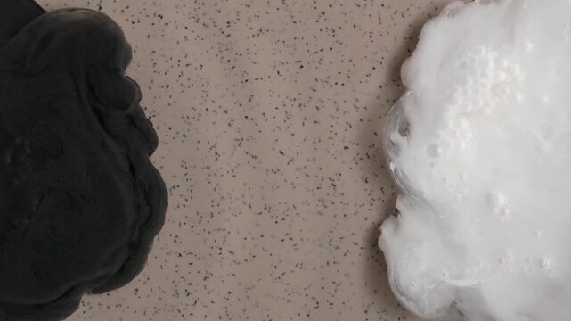 Black and white abstract liquid plumes spreading on speckled beige background