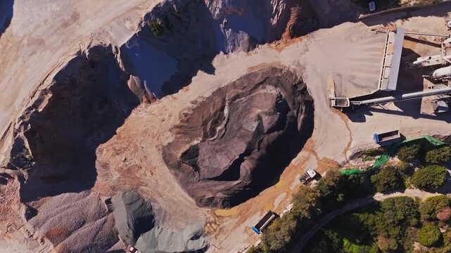 Aerial view of a stone quarry with a processing plant, asphalt machinery, and gravel piles surrounded by green vegetation in Manilva, Andalusia, Spain.