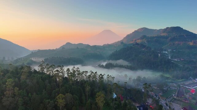 Aerial view of misty mountains and lush green hills at sunrise with fog in the valley in Pekalongan, Central Java, Indonesia.