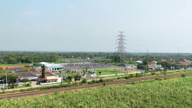 Aerial view of an electrical substation with high voltage power lines and a transmission tower near a railway track in Pekalongan, Central Java, Indonesia.