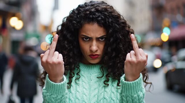 Angry Young Woman Showing Middle Fingers on a Blurred City Street, Ideal for Social Commentary and Emotional Storytelling.