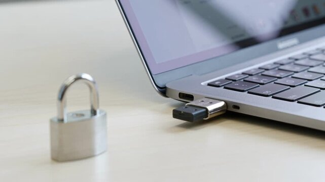 Close up of hand inserting a USB drive into a laptop next to a padlock symbolizing cybersecurity.