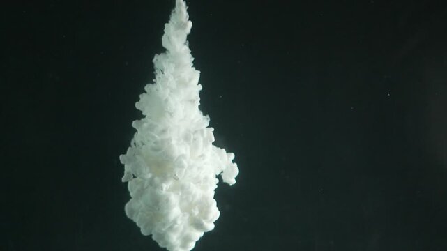 Abstract white ink cloud billowing and swirling in dark water against a black background