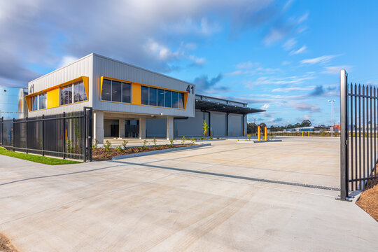 Secure industrial warehouse facility viewed through gated entrance with office accommodation, loading bays and large vehicle manoeuvring area.