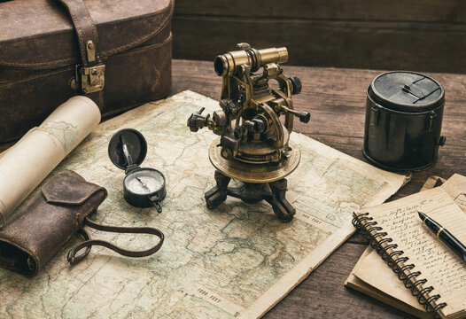 Vintage surveying equipment including a brass theodolite, compass, and old maps spread out on a rustic wooden table for historical navigation
