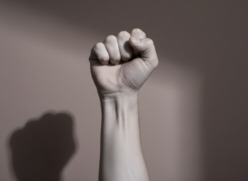 Clenched Fist Raised Vertically in a Gestue of Strength and Resilience Against a Muted Mauve Studio Wall with Ample Copy Space for Social Justice Editorial Use