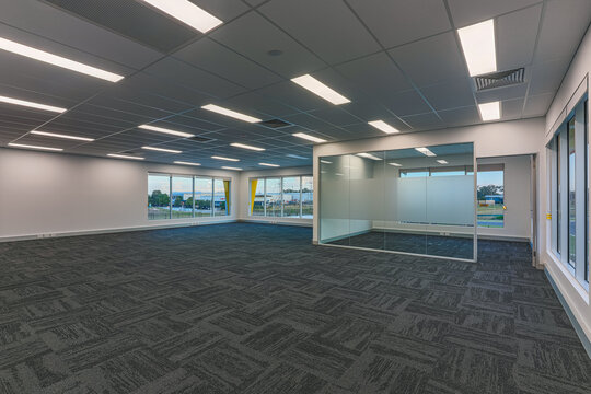 Empty commercial office interior with open workspace, large windows, carpet tile flooring and modern ceiling lights in a professional business setting.