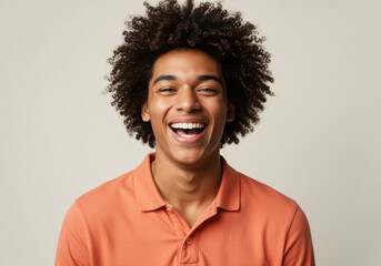 Fototapeta premium Joyful young man with curly hair laughing during a waist-up portrait for youth lifestyle, diversity marketing and wellness advertising, featuring a warm cream background