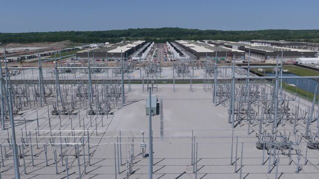 Aerial view of electrical substation with metal structures and power lines with giant Ai construction site in the background