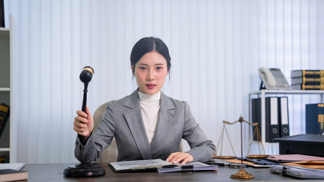 Asian women lawyer judge holding gavel sitting desk law office courtroom professional attorney legal justice workspace barrister solicitor counselor advocate