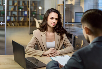 Fototapeta premium Client and advisor meeting for finance consultation. In a quiet office the manager explains banking options with paperwork and a laptop. Strong concept of client focused financial guidance.