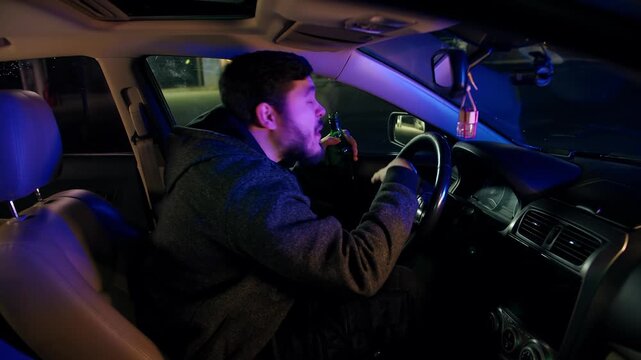 A drunk driver with a bottle of alcohol is surprised and indignant at being pulled over by police for breaking the law. Punishment for bearded caucasian man for drunk driving at night. Scene from car