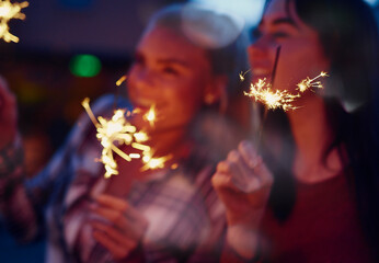 Obraz premium Night, sparklers or happy women with celebration for new year festivity, birthday party or holiday. Excited, female people or fireworks with smile in late evening for fun event, festival or memory