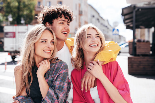Group of young three stylish friends posing in the street. Fashion man and two cute female dressed in casual summer clothes. Smiling models having fun. Cheerful women and guy outdoors