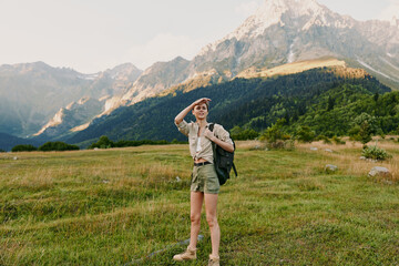 Obraz premium Young woman hiking in a bright meadow beside majestic mountains, carrying a backpack, casual outdoor attire, capturing a spontaneous travel moment in nature