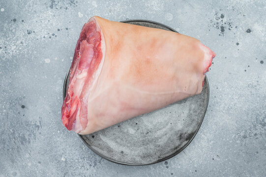 Raw pork knuckle hock showing rind surface, subcutaneous fat and exposed muscle tissues on stone plate with thyme for technical culinary visuals.