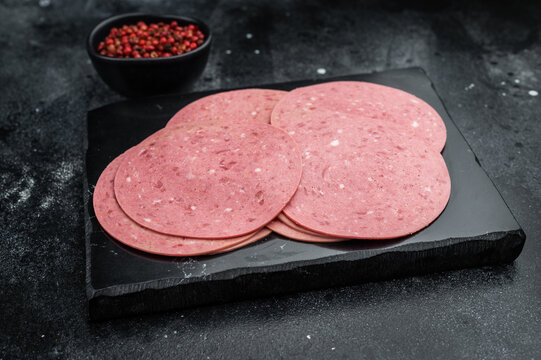 Thin round slices of Turkish beef salam arranged on a slate board with red pepper on dark stone background ideal for deli and food stock use