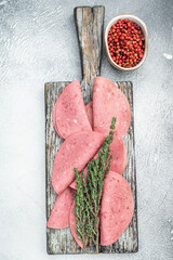 Thin slices of Turkish beef salam on rustic wood with thyme and pepper on bright textured background ideal for deli and food stock use © Mironov