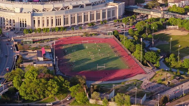 High angle shot showing Yankee Stadium and adjacent sports complex in the South Bronx, with people playing soccer and running on the track during a warm, sunny afternoon