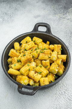 Roasted baby corn sliced into pieces with seasoning and thyme in skillet overhead on textured background