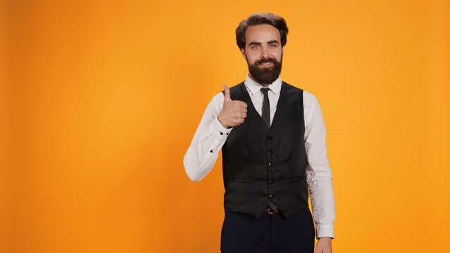 Trendy valet raises thumbs up gesture in studio to symbolize satisfaction and to indicate acceptance. Professional catering providers giving their seal of approbation on camera.