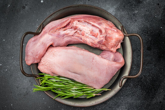 Whole raw uncooked pork tongue offal in skillet with herbs and vintage fork top view on dark background perfect for cuisine and butchery themes