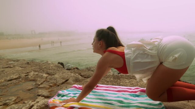 Cliffside yoga flow woman practicing downward stretch on towel