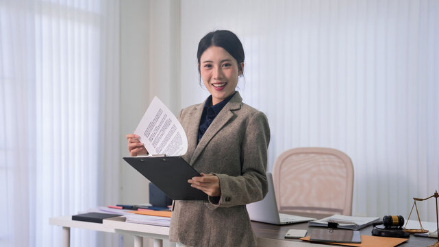 young Asian lawyer woman holding document folder standing modern office workspace business professional legal consultant reviewing contract papers law firm